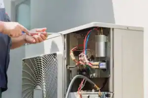Technician using a screwdriver to open the service panel of an outdoor air conditioning unit.