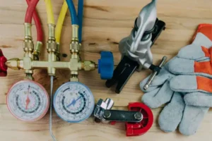 HVAC manifold gauges, pipe cutter, flaring tool, and protective gloves arranged on a wooden surface.