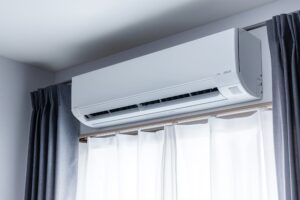 Wall-mounted ductless mini-split air conditioner installed above a window with curtains.